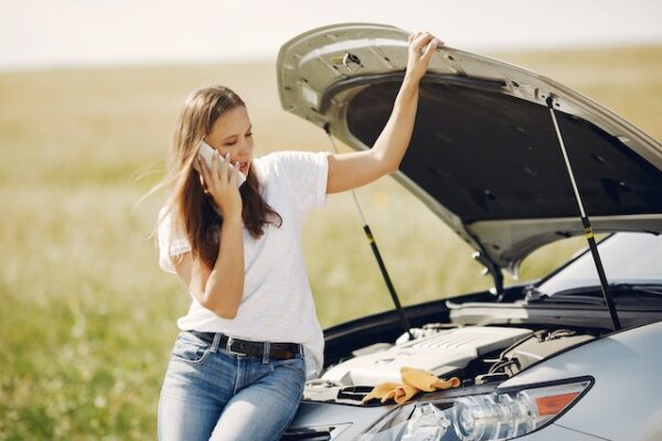 Woman on the phone with car hood up.